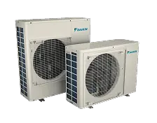 Two outdoor HVAC condenser units labeled "Daikin" positioned side by side on a plain, light background.
